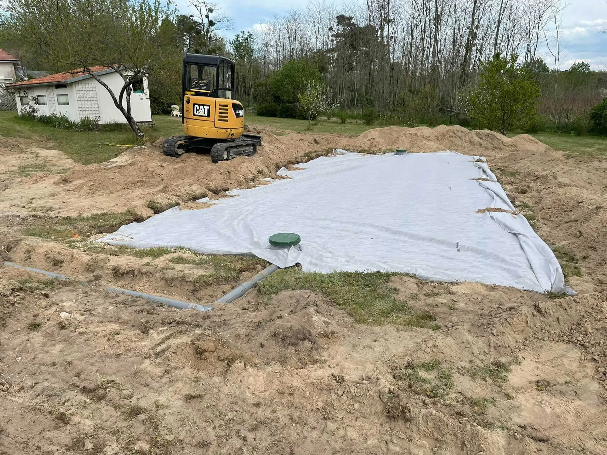 Chantier de terrassement avec bâche protectrice et mini-pelle en arrière-plan.